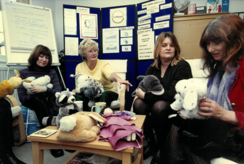 Four women sat in a row holding toys.